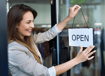 Woman turns a sign to open on front door of her business storefront